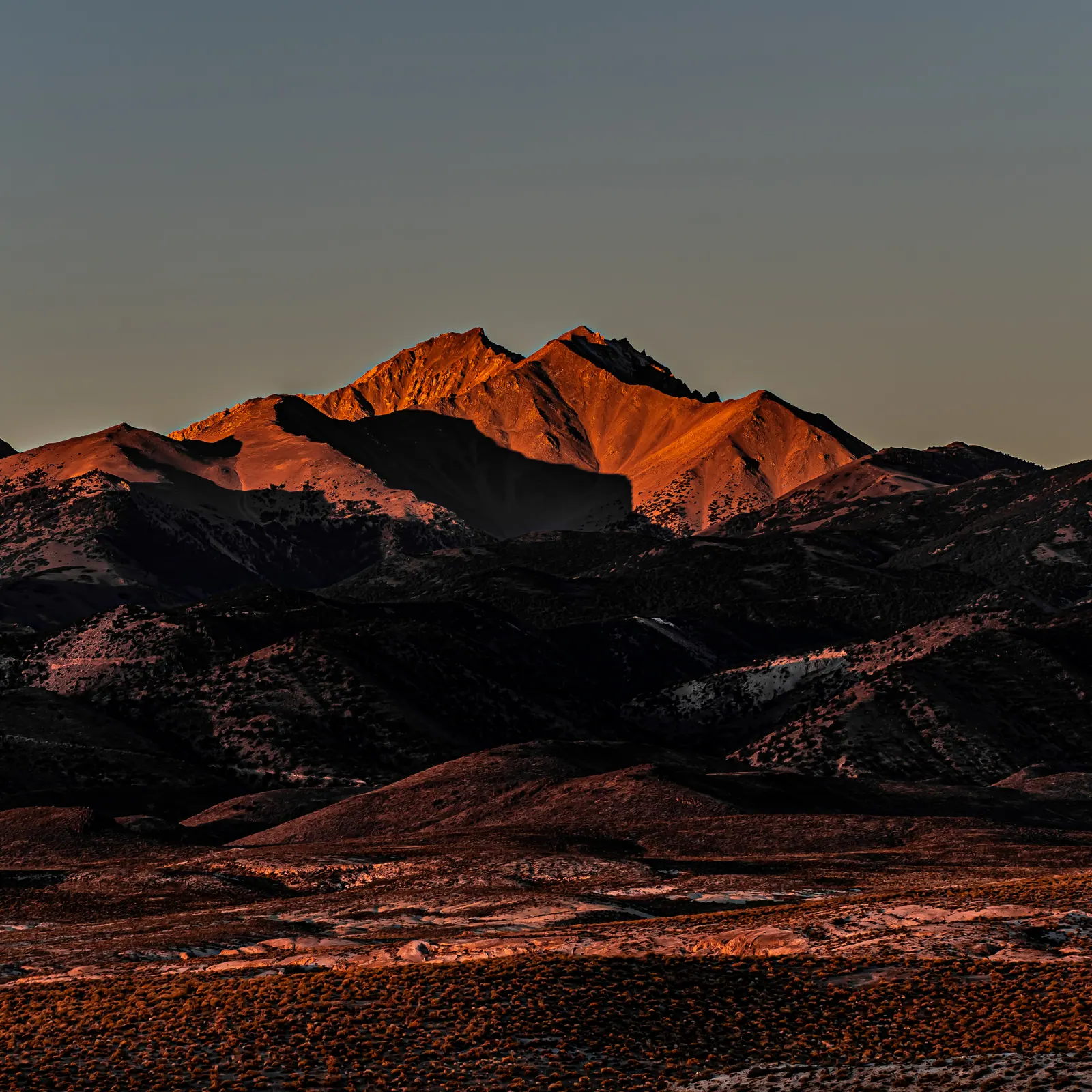 Low sunlight turns a distant mountain ridge red above a dark desert foreground.