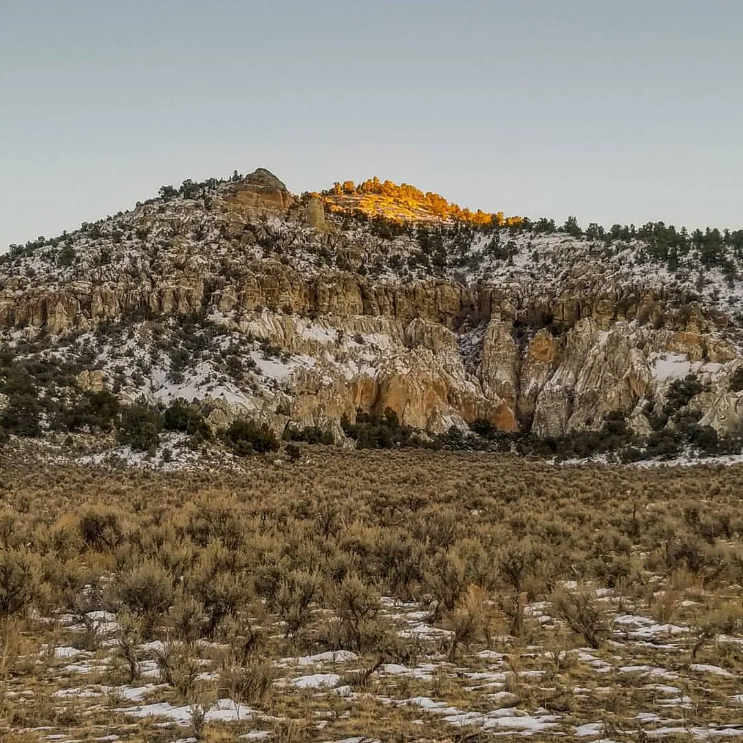 A snow-dusted hillside rises toward a small patch of warm light.