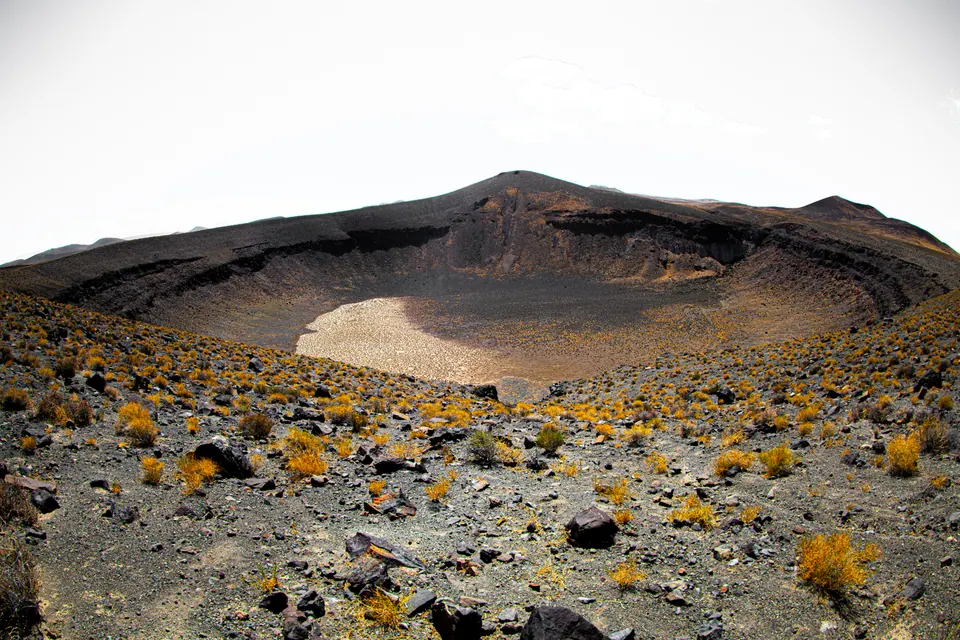 Dark volcanic ground curves around the rim of a broad, shallow crater.