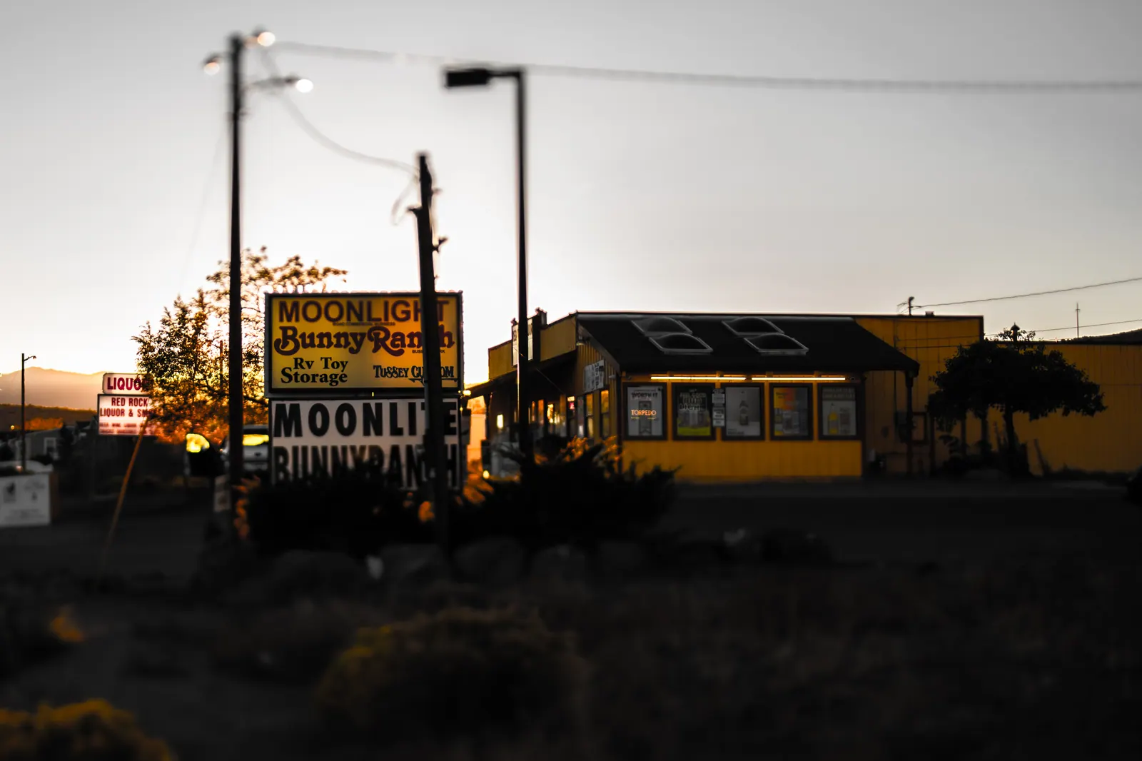 An old roadside sign stands beside a low building in fading evening light.