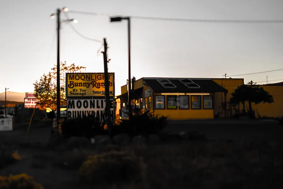 An old roadside sign stands beside a low building in fading evening light.