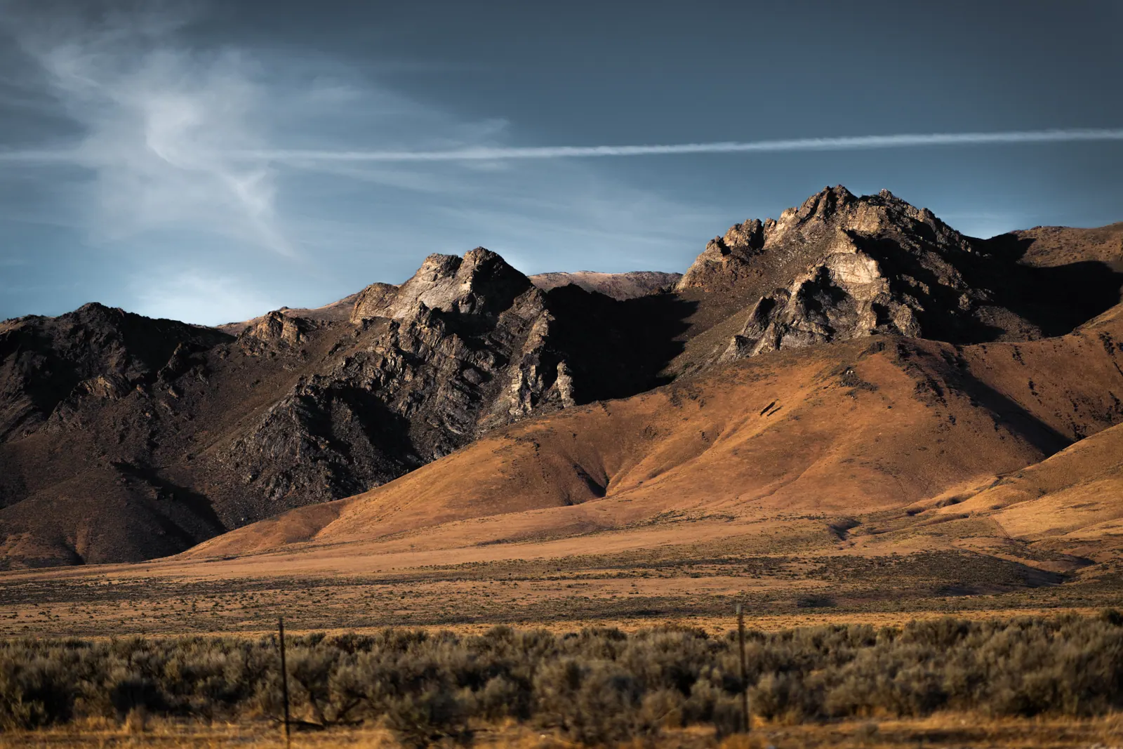 Warm brown mountain slopes rise above a flat expanse of golden grass under a pale blue sky.