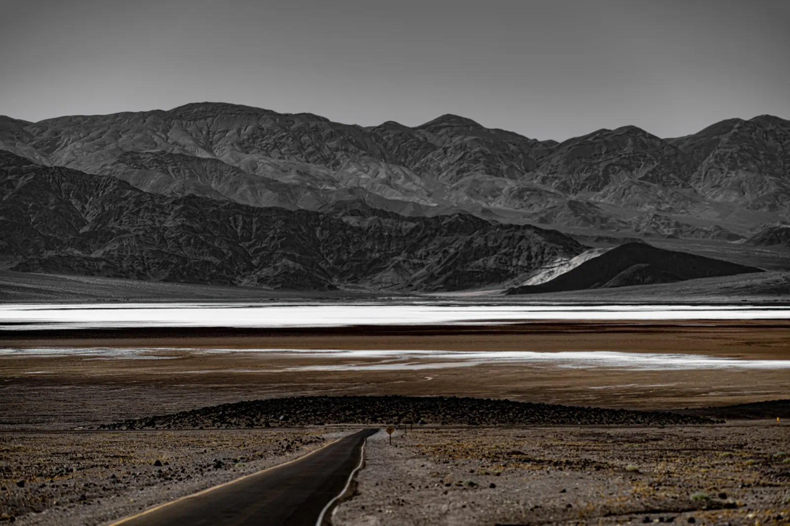 Pale bands cross a broad desert basin beneath dark, folded mountains.