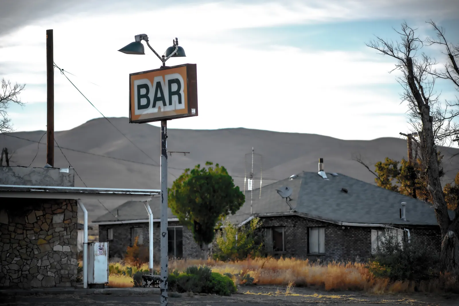 A simple bar sign rises above a low building and a quiet street.