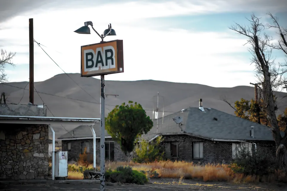 A simple bar sign rises above a low building and a quiet street.