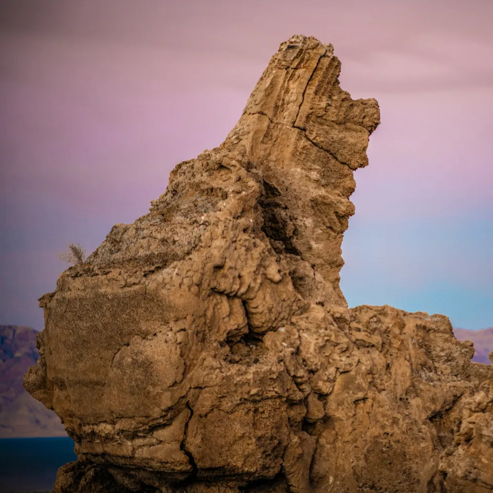 A tall weathered rock formation rises against a soft pink and blue sky.
