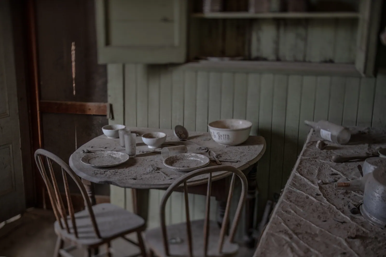 Cups and bowls remain on a small table in an abandoned wooden kitchen.