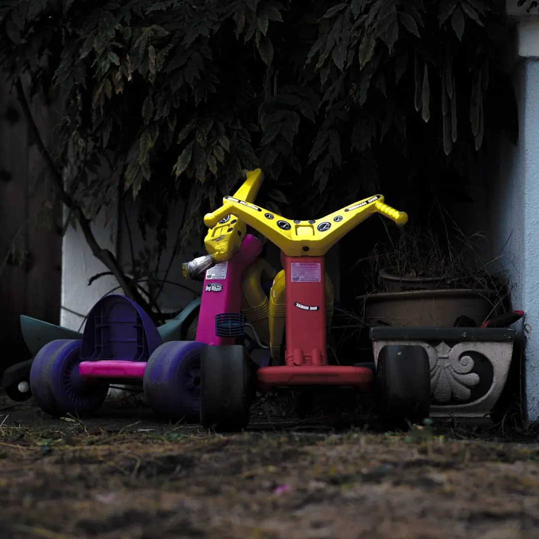 Brightly coloured plastic toys sit beneath a dark tree beside an old wall.