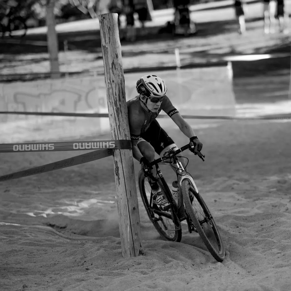 A cyclist leans into a turn across dusty ground in black and white.