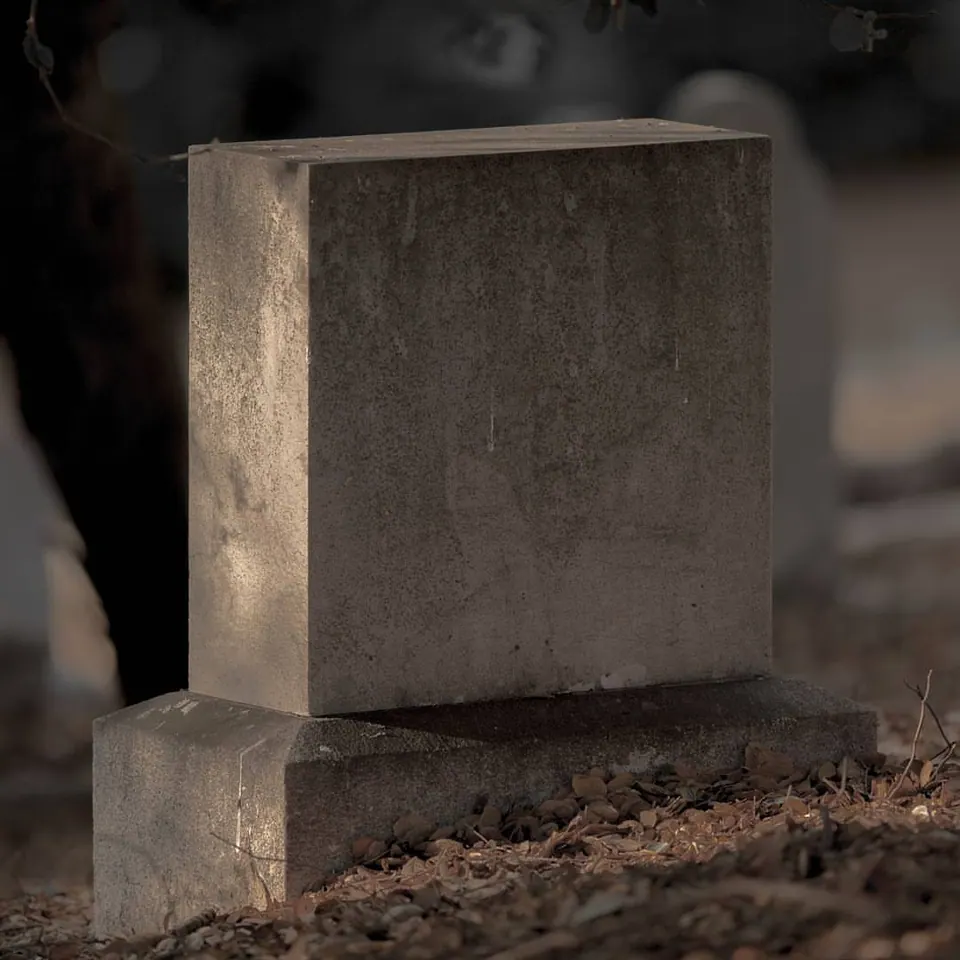 A simple rectangular stone marker stands among fallen leaves and shadows.