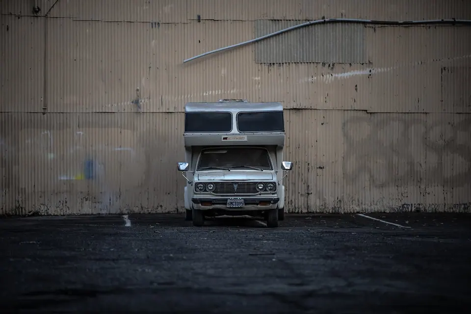 A small van stands below the tall metal wall of an industrial building.