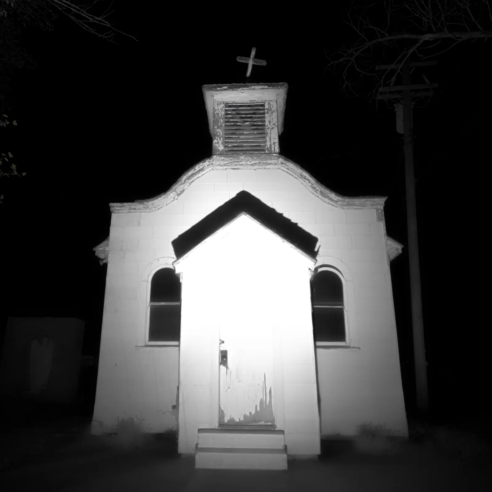 A small white church stands brightly lit against a deep black sky.