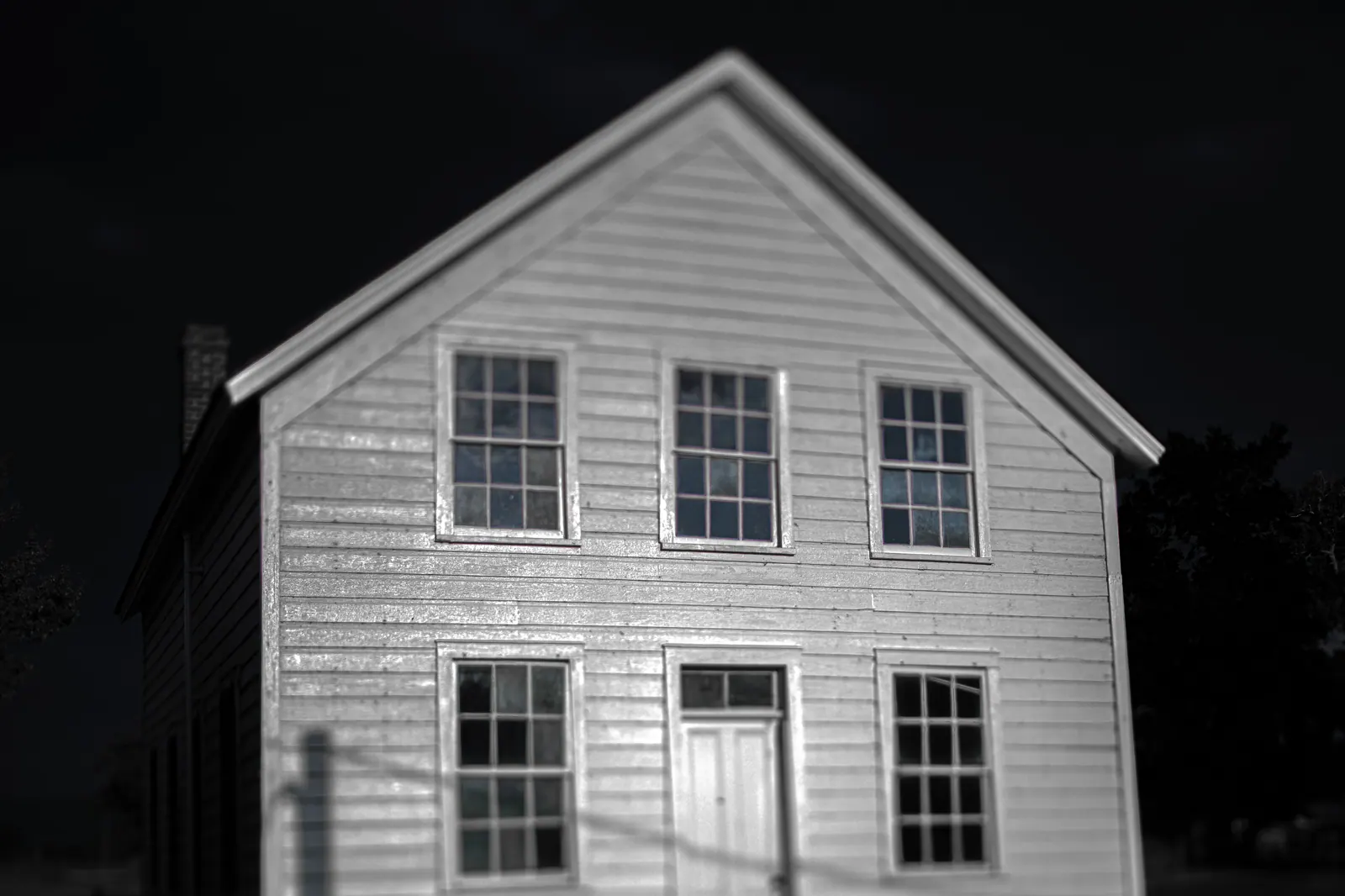 A simple white wooden house stands out against a dark background in black and white.