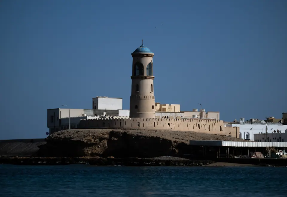 A white waterfront tower rises above blue water beneath a clear sky.