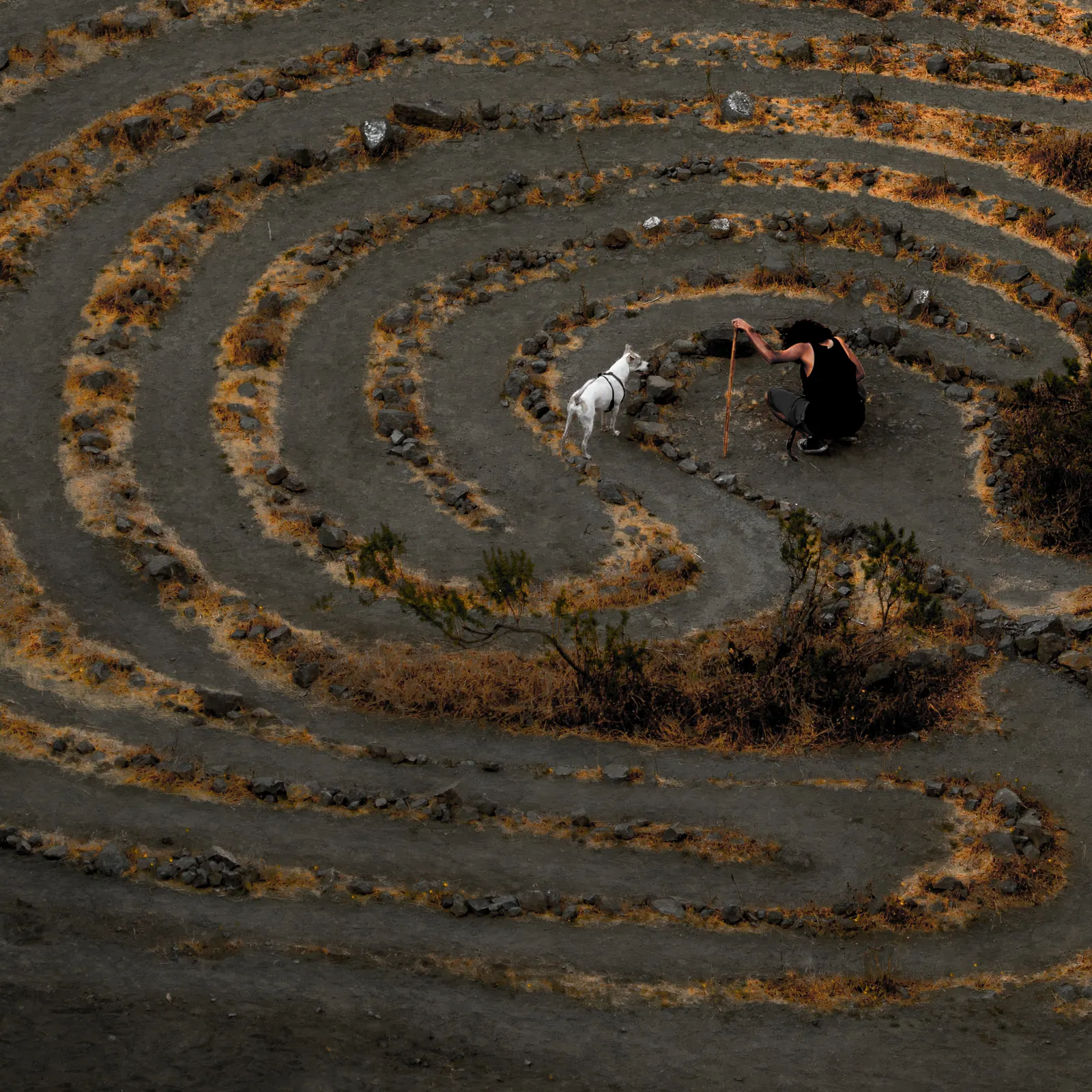 A circular labyrinth is traced into dry ground, with a small figure near its centre.