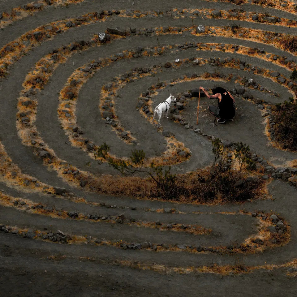 A circular labyrinth is traced into dry ground, with a small figure near its centre.