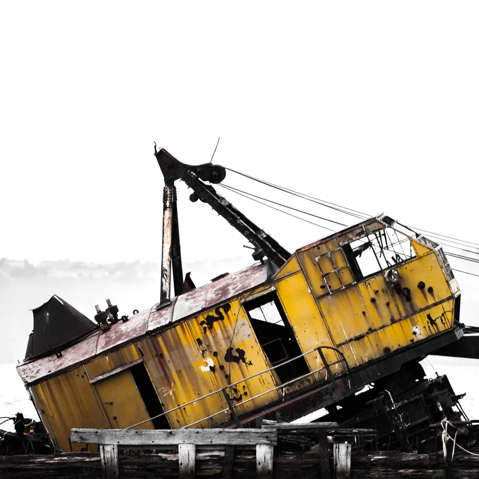 A weathered yellow vessel tilts beneath a pale sky, showing dark ropes and metalwork.