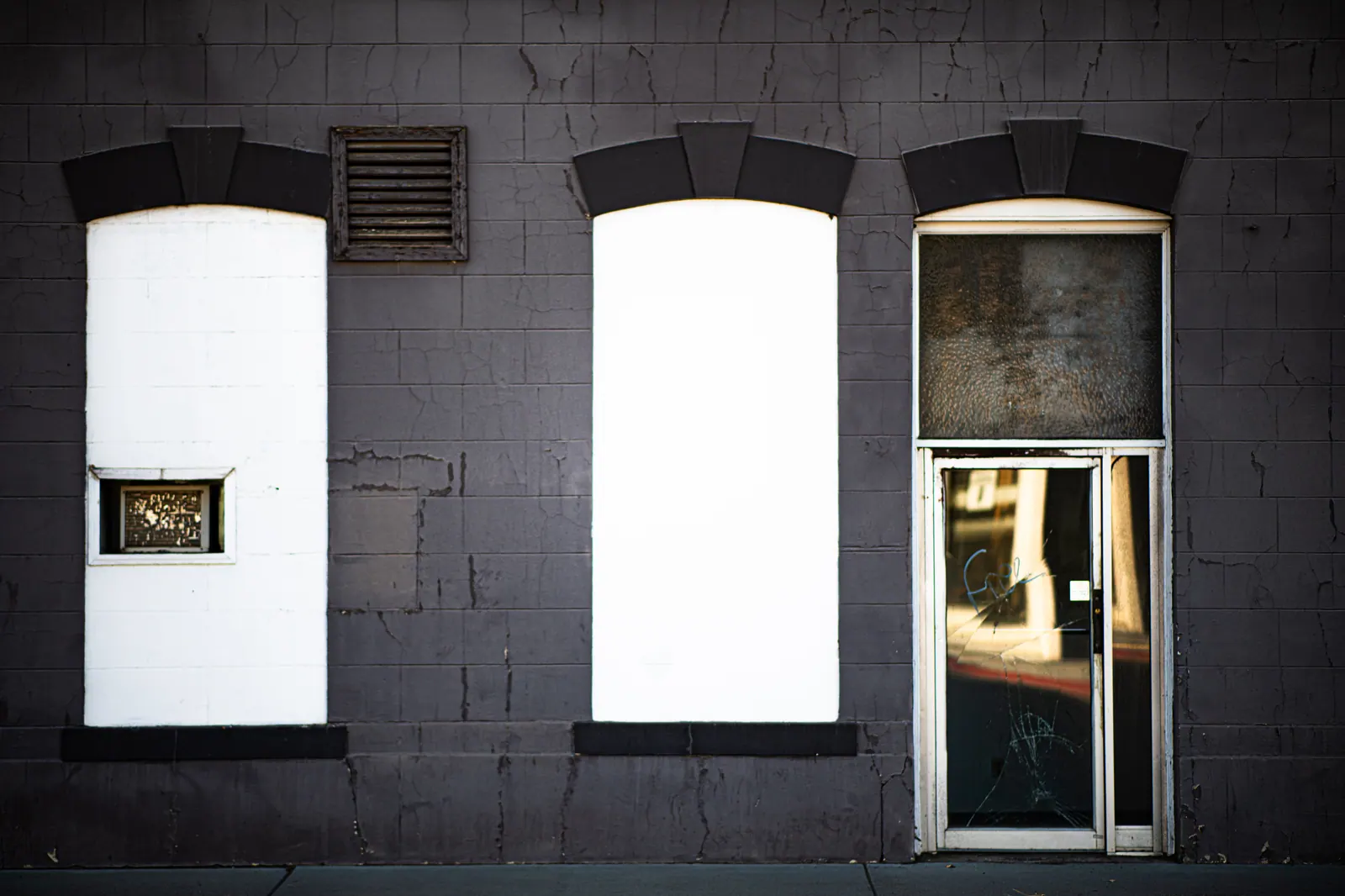 Two boarded windows and a glass door break up a dark shopfront.