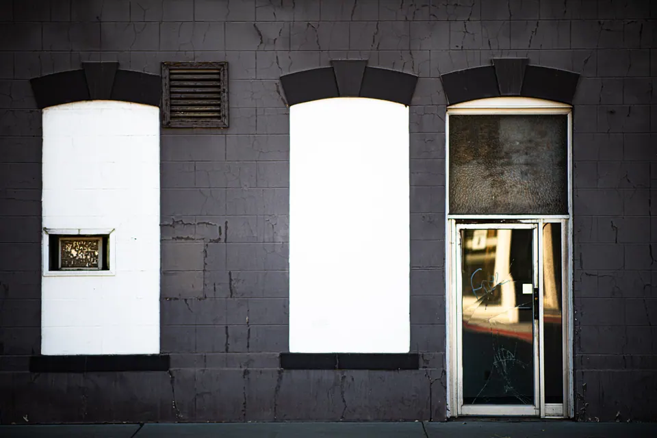 Two boarded windows and a glass door break up a dark shopfront.