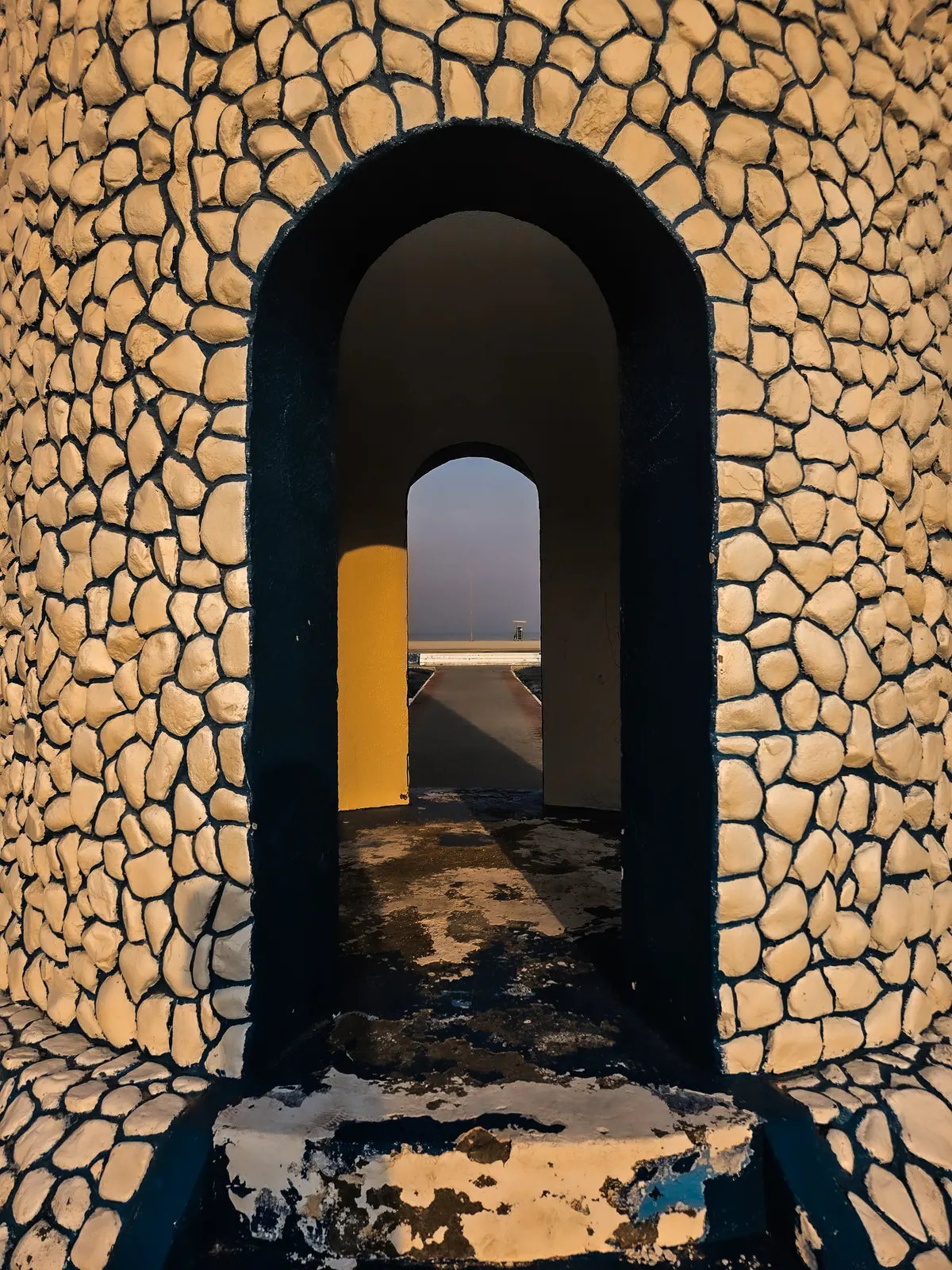 Warm sunlight crosses a stone archway, revealing another opening beyond it.