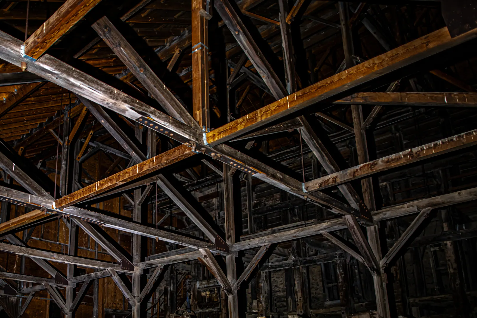 Heavy wooden rafters crisscross the dark interior of a large old building.