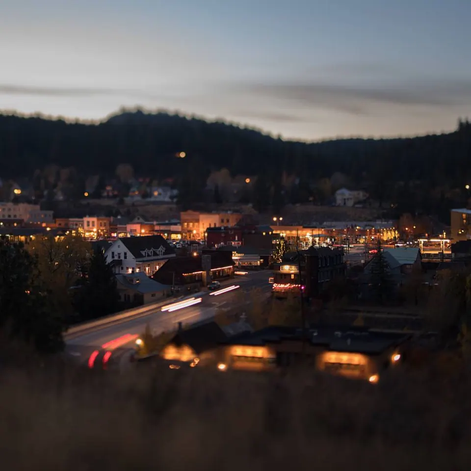 Small pools of warm light brighten a town beneath dark wooded hills.