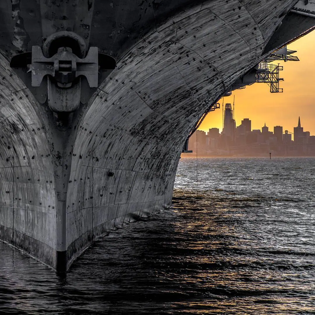 The underside of a broad concrete arch frames warm light above a river.