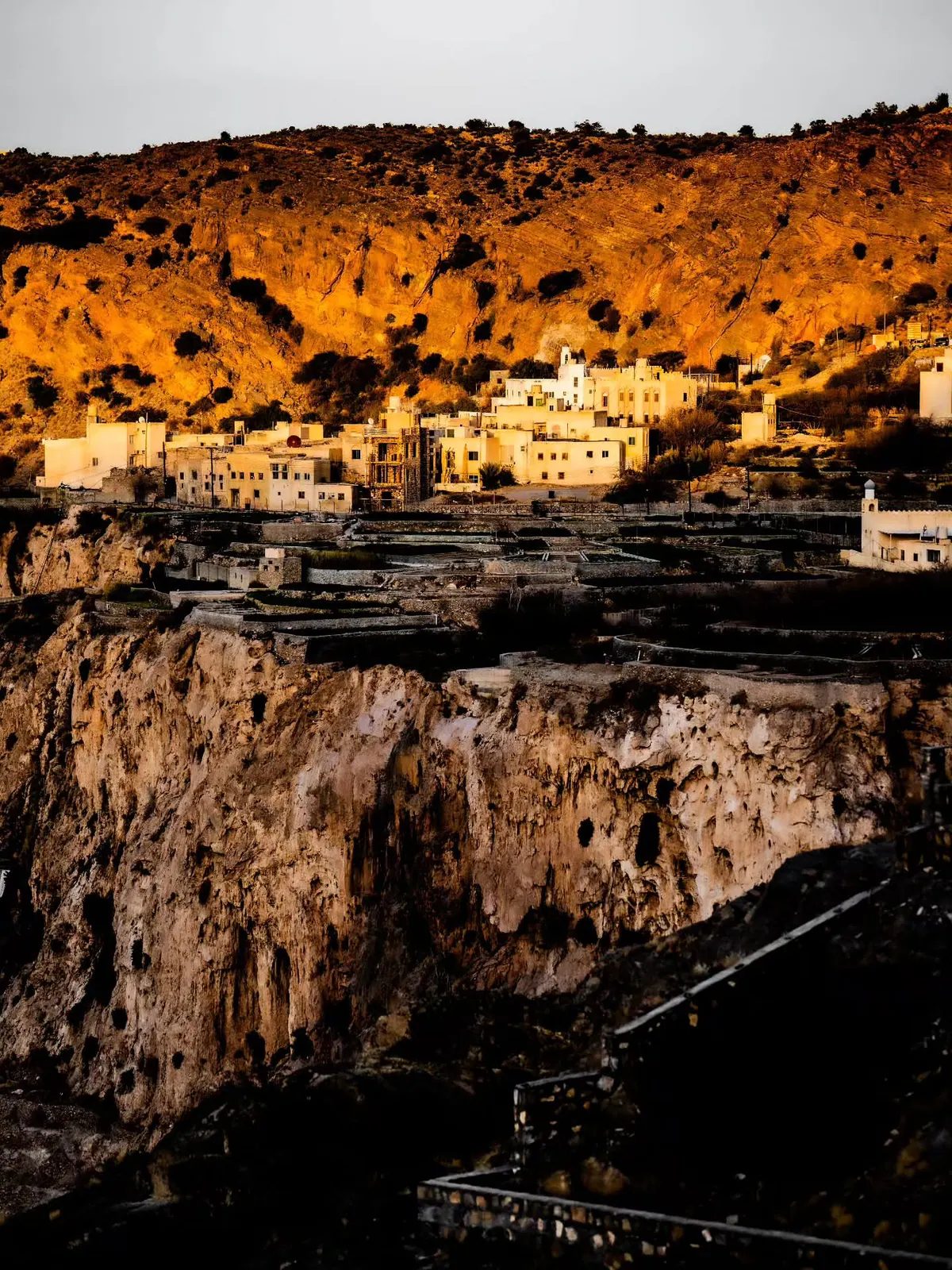 A pale village sits below a glowing ochre hillside as the valley falls into shadow.