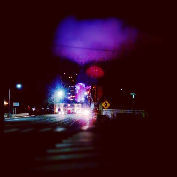 A violet glow hangs above a dark road dotted with small lights.