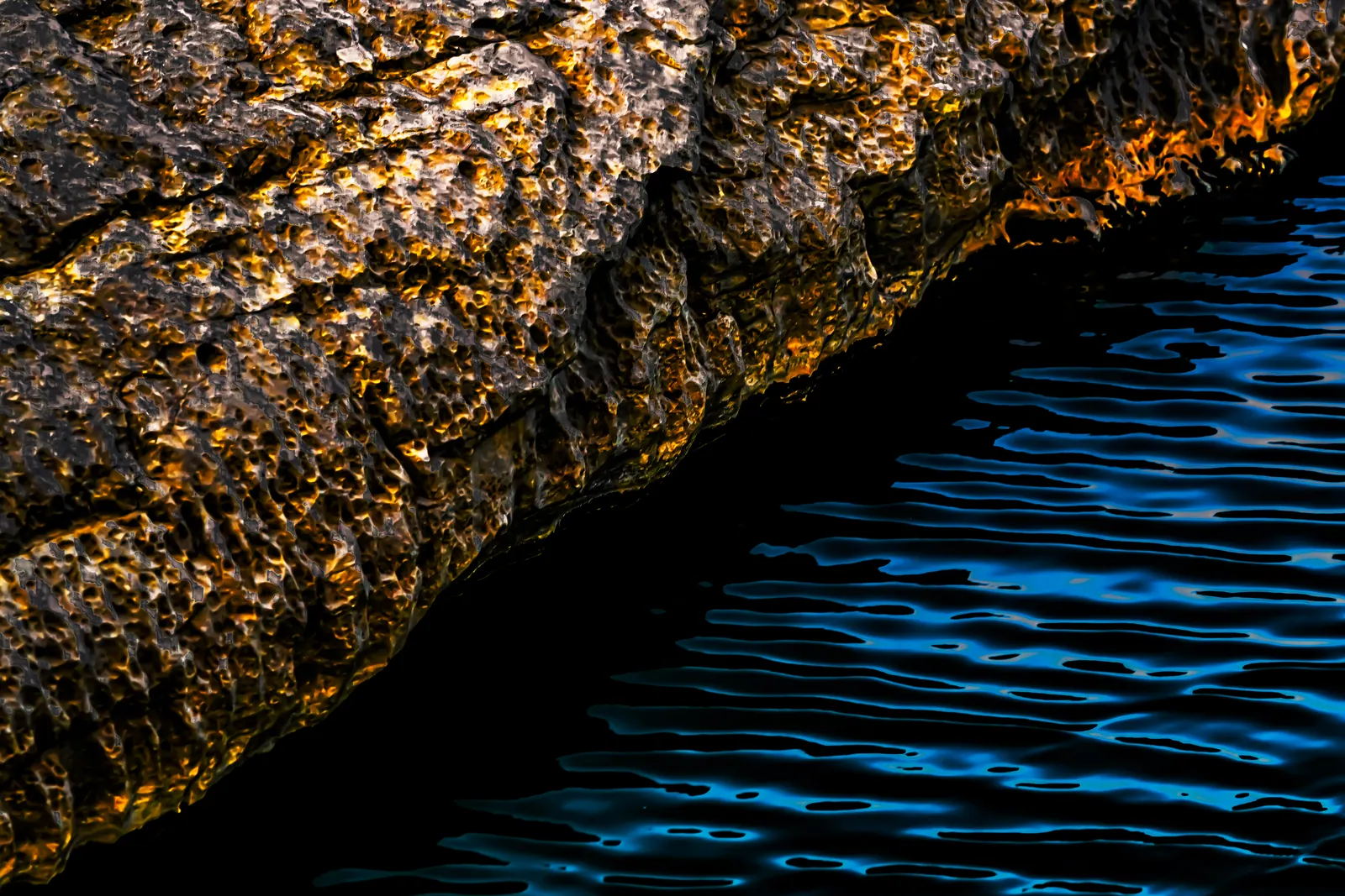 Sunlight catches the rough edge of a rock above deep blue ripples.