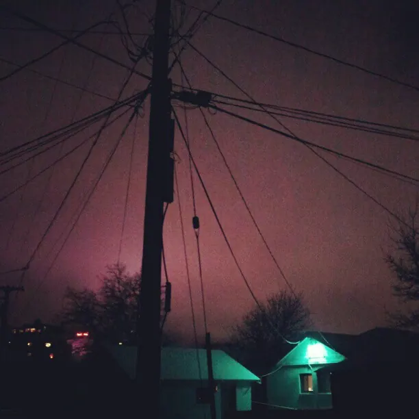 Utility wires cross a purple evening sky above a small illuminated building.