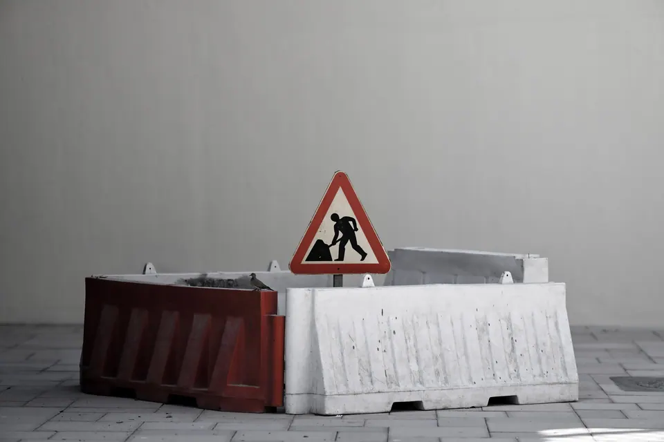 A roadworks sign stands above red and white barriers in pale mist.